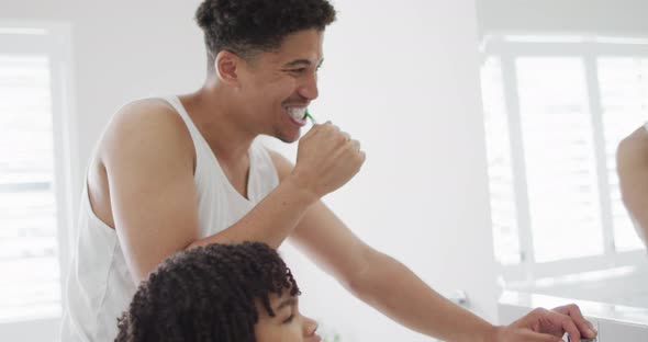 Happy biracial man and his son washing teeth in bathroom