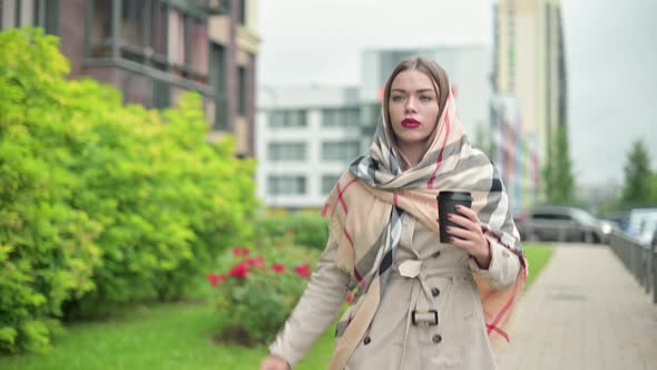 woman in coat with a glass of coffee in her hand moves quickly along the street