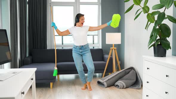 Woman in Headphones Cleaning the House and Having Fun Dancing with a Broom and Washcloth