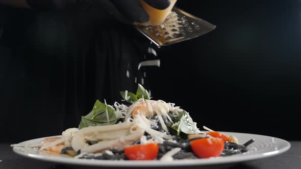 Chef Grating Hard Cheese on Freshlycooked Black Seafood Pasta