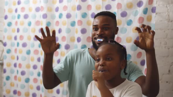 African Father and Toddler Girl Brushing Teeth Together in Bathroom