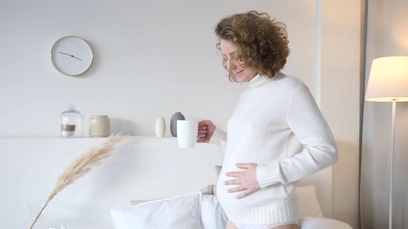 Happy Lifestyle Of Pregnant Woman Dancing With Cup Of Tea In Bedroom.