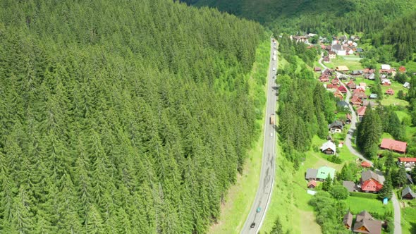 Aerial View of the Road with Driving Cars and Truck in the Mountains with High Green Fir Foliar Pine