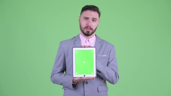 Happy Young Bearded Businessman Talking While Showing Digital Tablet