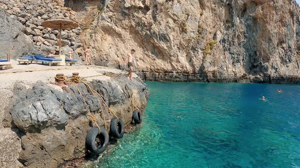 Athletic Man Cliff Jumping into the Sea. Slow Motion. Young Man Jumps off Cliff Into Blue Ocean