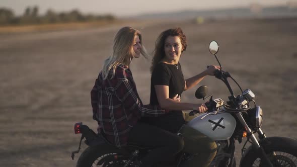 Attractive Young Woman Motorcyclist with His Girlfriend Riding a Motorcycle in a Desert on Sunset or