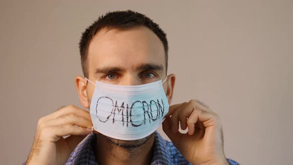 A European man against a gray background wears a medical mask over his face with Omicron