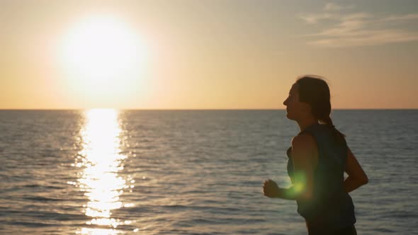 Motivated fitness female in sportswear runs along beach promenade at sunset. Running concept