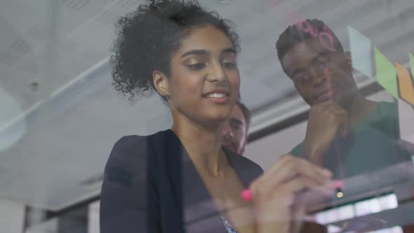 Diverse colleagues using memo notes and writing on glass wall having a discussion