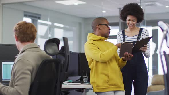 Diverse smiling male and female business colleagues using tablet and discussing paperwork in office