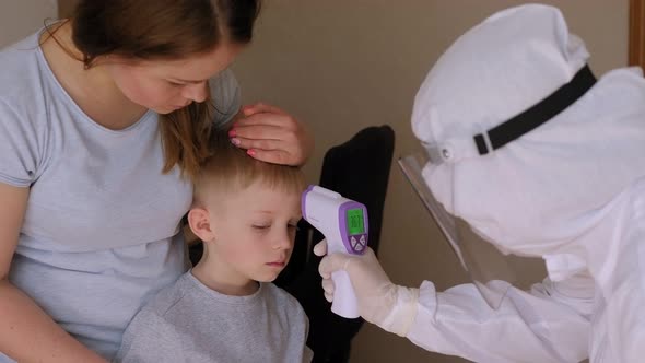 A Doctor in a Protective Suit Measures the Temperature to a Small Boy at Home