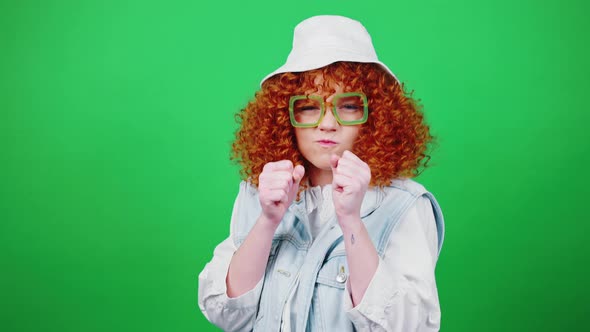 Playful Redhead Curly Lady in Glasses and Panama Hat Joking Boxing to Camera and Laughing Green