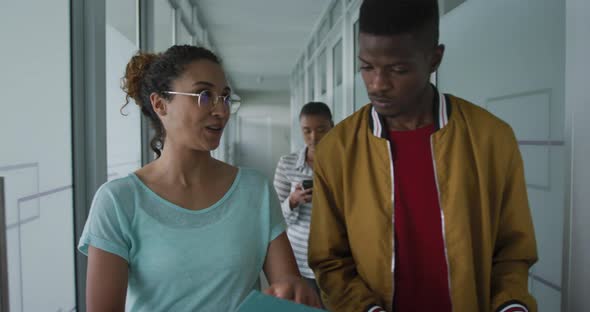 Happy diverse male and female creative colleague walking in workplace corridor and talking