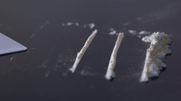 Making lines of cocaine with a credit cand. Cocaine lines shots on a black table glass.