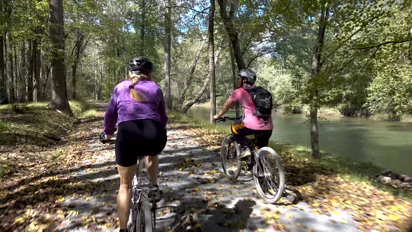 Mother and teenage son biking side by side on a rural gravel road with a river to their right side.