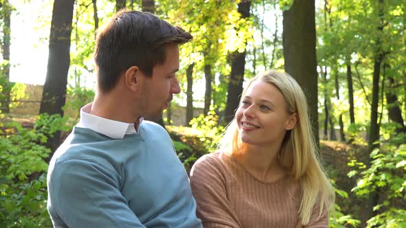 A Young Attractive Couple Hugs and Talks on a Bench in a Park on a Sunny Day, Closeup