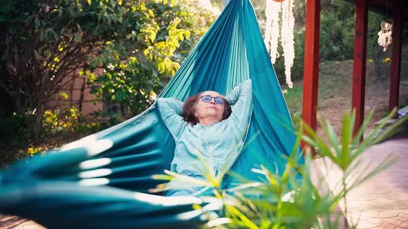 A Mature Adult Woman Relaxes Lying in a Hammock on a Terrace