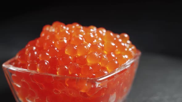 A Serving of Selected Red Caviar Rotates on a Black Background in a Transparent Glass Bowl