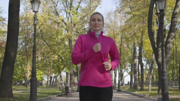Young Caucasian Woman in Sportswear and Headphones Running in the Autumn Park. Female Runner