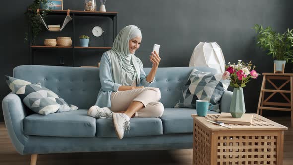 Smiling Young Muslim Woman Making Online Video Call Looking at Smartphone Screen in Nice Apartment