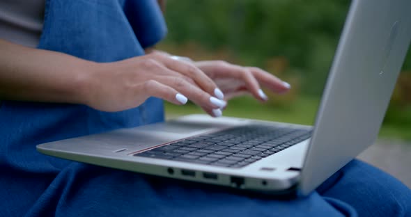 Female Hands Are Typing on Keyboard of Notebook Outdoors, Close-up of Her Palms and Fingers