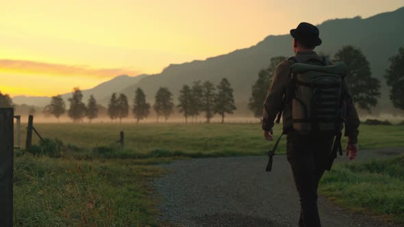 Man Walking Along Country Path Towards Misty Landscape At Sunrise