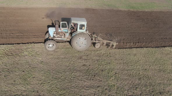 Side View of Tractor Riding in Sunlight Along Field