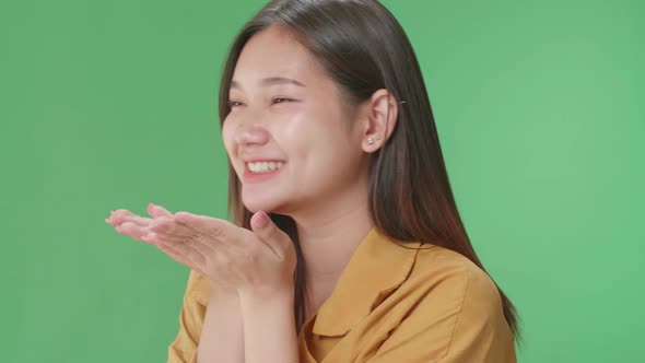 Close Up Of Side View Of A Smiling Asian Woman Blowing Kisses To A Camera In The Green Screen Studio