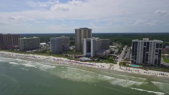 Dolly shot of drone slowly descending above ocean looking towards ocean front resorts