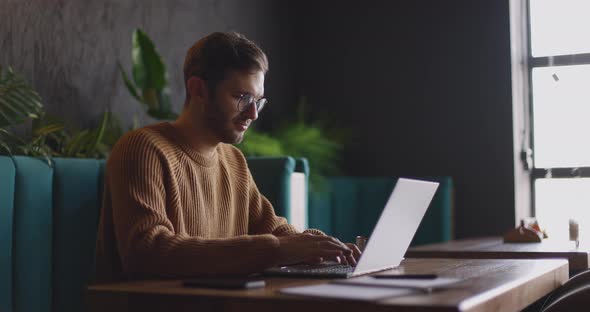 Side View of Man Who Sits in Cafe in Daytime and Using the Laptop for the Remote Work