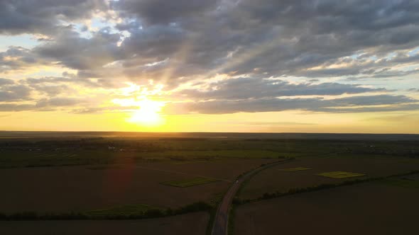 Aerial View of Intercity Road with Fast Driving Cars Between Farmland Fields at Sunset