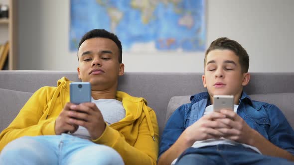 African-American and Caucasian Teens Scrolling Smartphones, Having Leisure Time