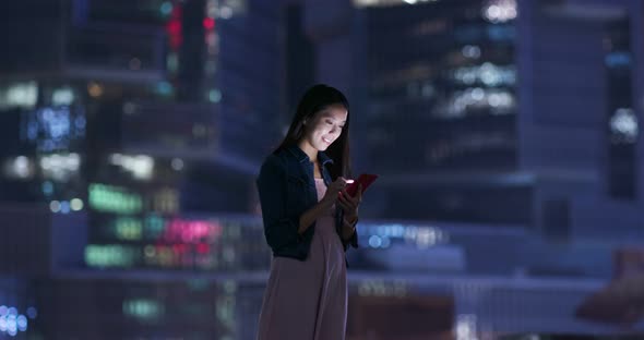 Woman look at mobile phone over business tower background at night