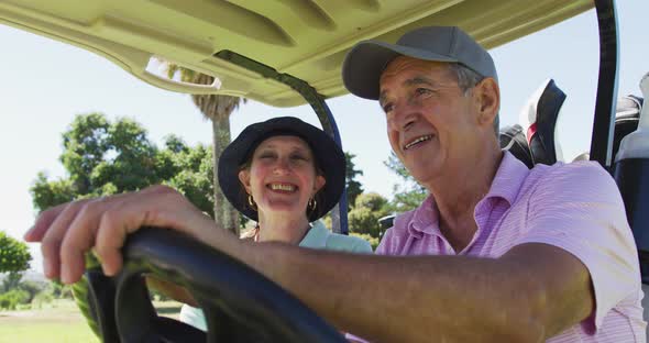 Caucasian senior couple driving a golf cart with clubs on the back at golf course