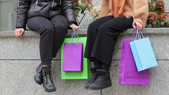 Two Unrecognizable Women Shoppers Sitting on Street in City Girlfriends After Shopping Discounts on