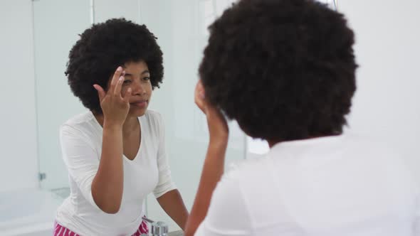 African american woman touching her face while looking in the mirror at bathroom