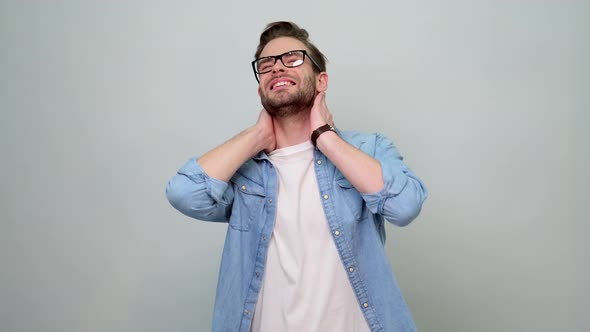 Bearded guy wearing jeans shirt looking exhausted, rubbing painful neck