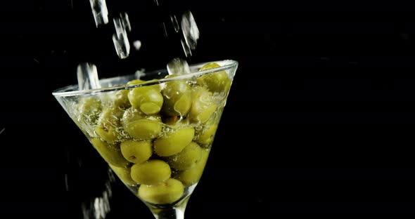Cocktail being poured into the glass full of olives