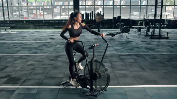 Young female athlete trains cardio on a bicycle with a fan, cardio and endurance training