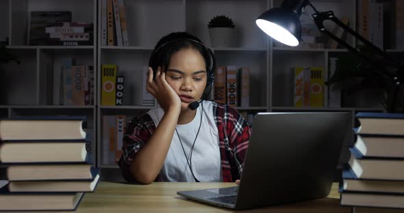 Tired female in headphones and glasses learning with laptop at night