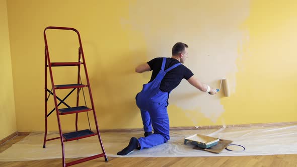 Young worker painting wall in room.