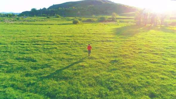 Flight Over Sport Man at Perfect Green Grass Meadow. Sunset in Mountain