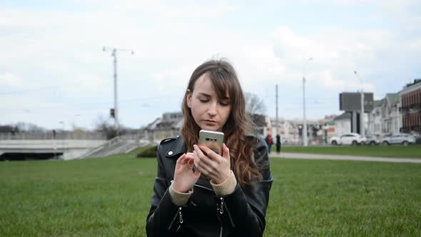 Girl Student Sits on the Lawn and Communicates with Friends Via the Internet