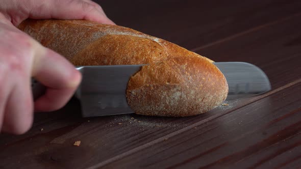 Chef Cuts Homemade Crispy French Baguette Bread Into Slices with Kitchen Knife on Wooden Board