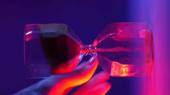 Man Hand Turns Over Glass Hourglass in Blue Red Light