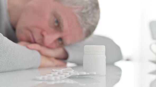 Depressed Sick Old Man Looking at Medicines on a Table