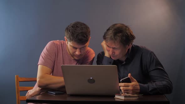 Young and Mature Men Work on Modern Notebook at Table