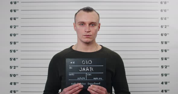Portrait of Male Criminal Person Holding Sign for Photo in Police Department