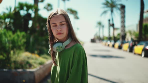 Serious blonde woman in headphones wearing green t-shirt walking