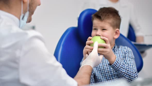 Male Dentist in Uniform Giving Fresh Green Apple to Happy Child